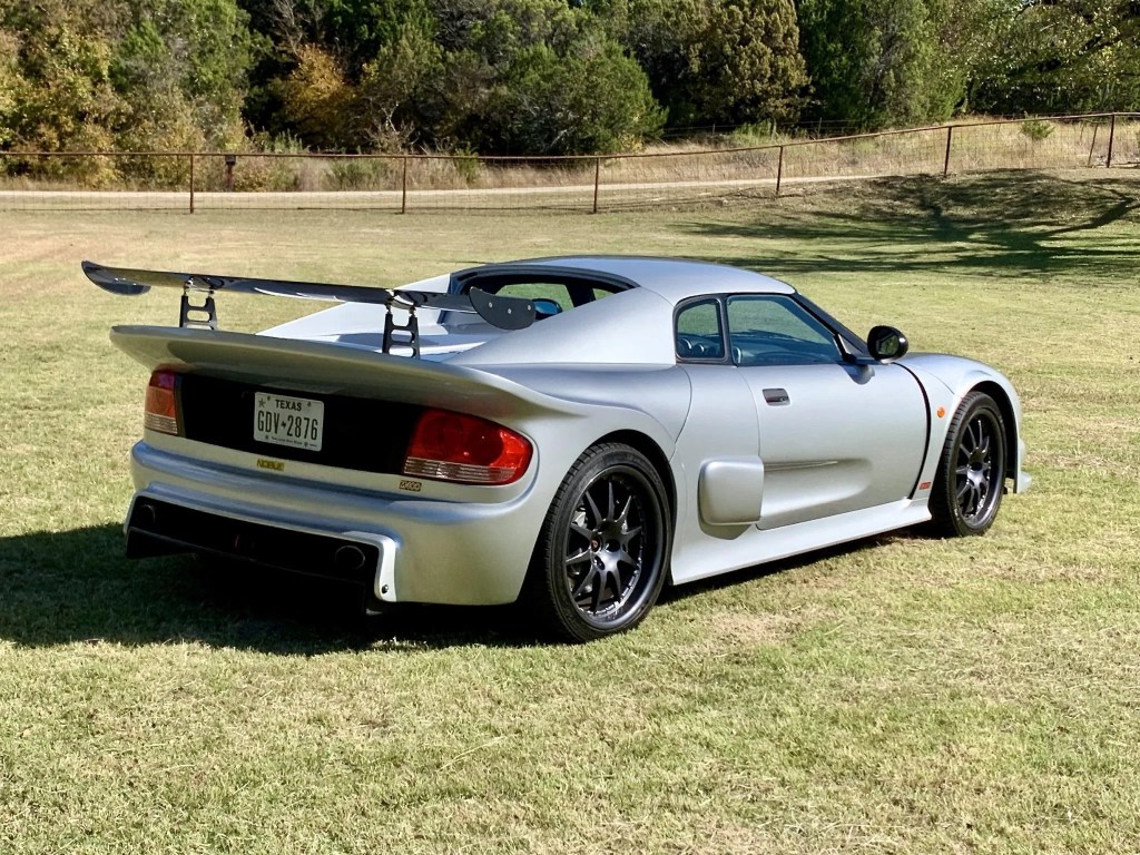 The rear 3/4 view of a silver 2005 Noble M400 in a grassy field