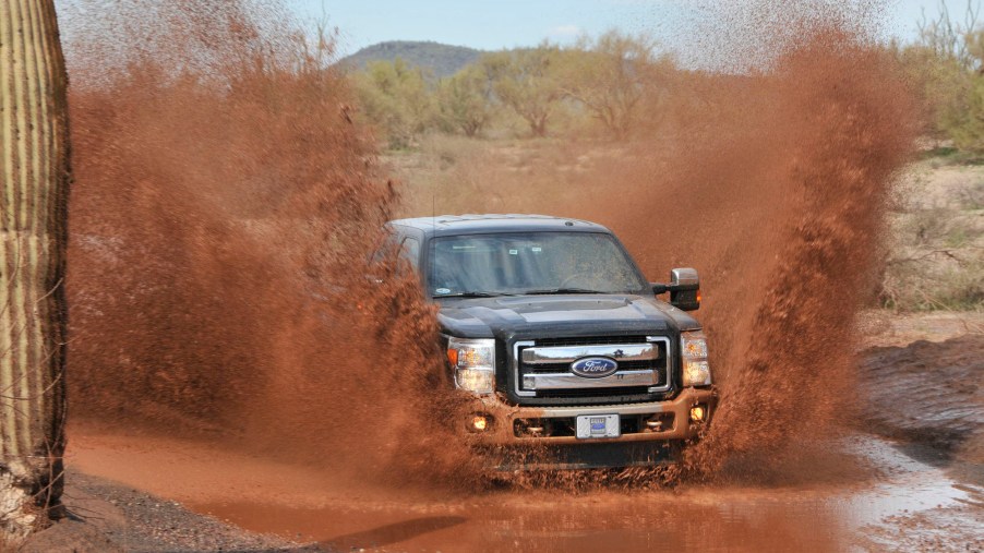 A black 2011 Ford F-250 Super Duty Power Stroke diesel pickup truck drives through mud