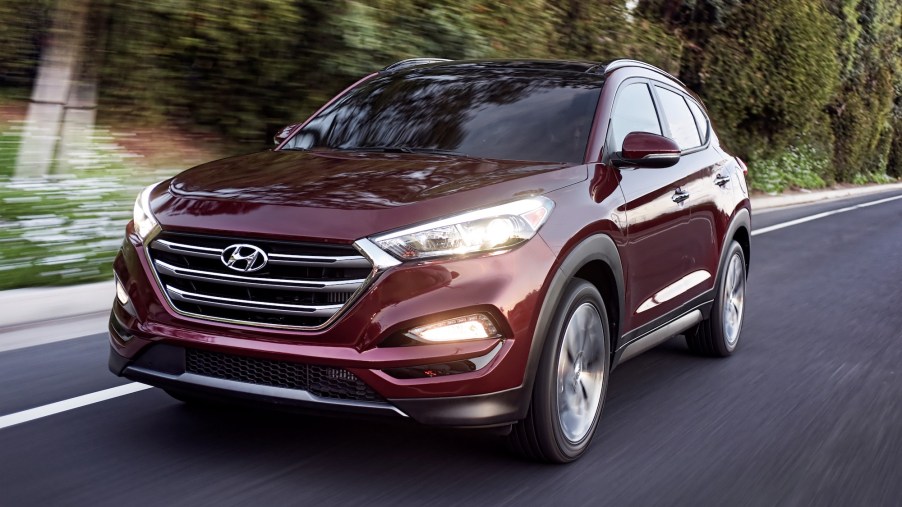 A maroon 2016 Hyundai Tucson travels on a highway lined by foliage