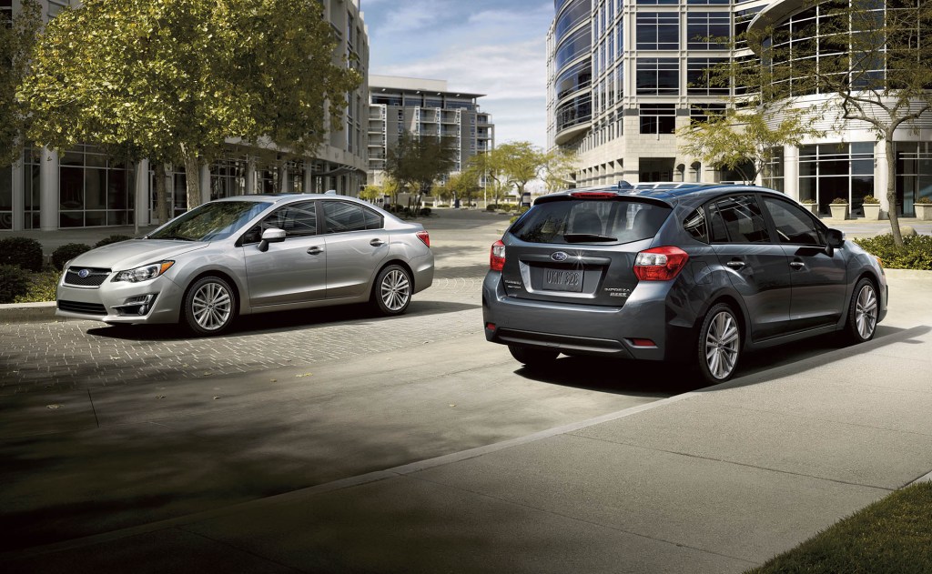A silver 2016 Subaru Impreza Sedan parked next to a grey 2016 Subaru Impreza Hatchback in a city street