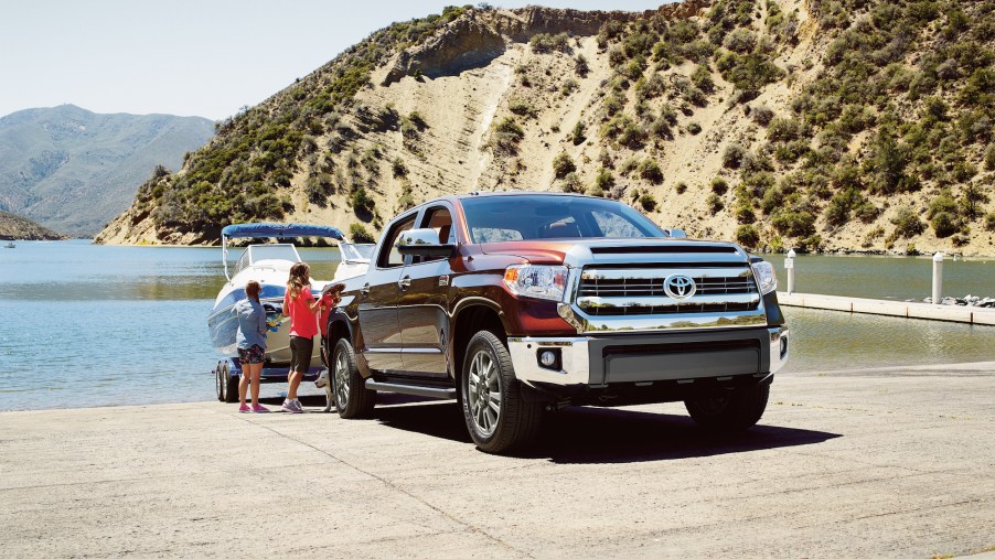 Two children stand next to a maroon 2016 Toyota Tundra towing a boat on a boat ramp overlooking a lake and mountains