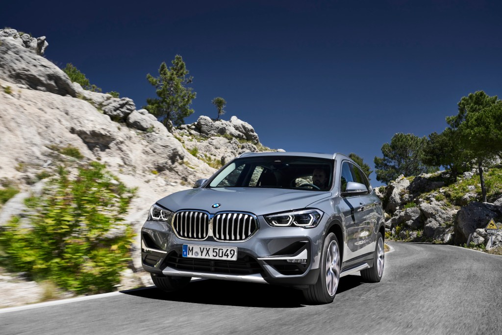 A silver 2020 BMW X1 European model travels on a paved road on a rocky hill