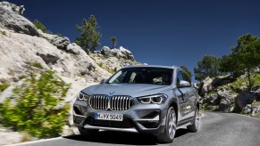 A silver 2020 BMW X1 European model travels on a paved road on a rocky hill