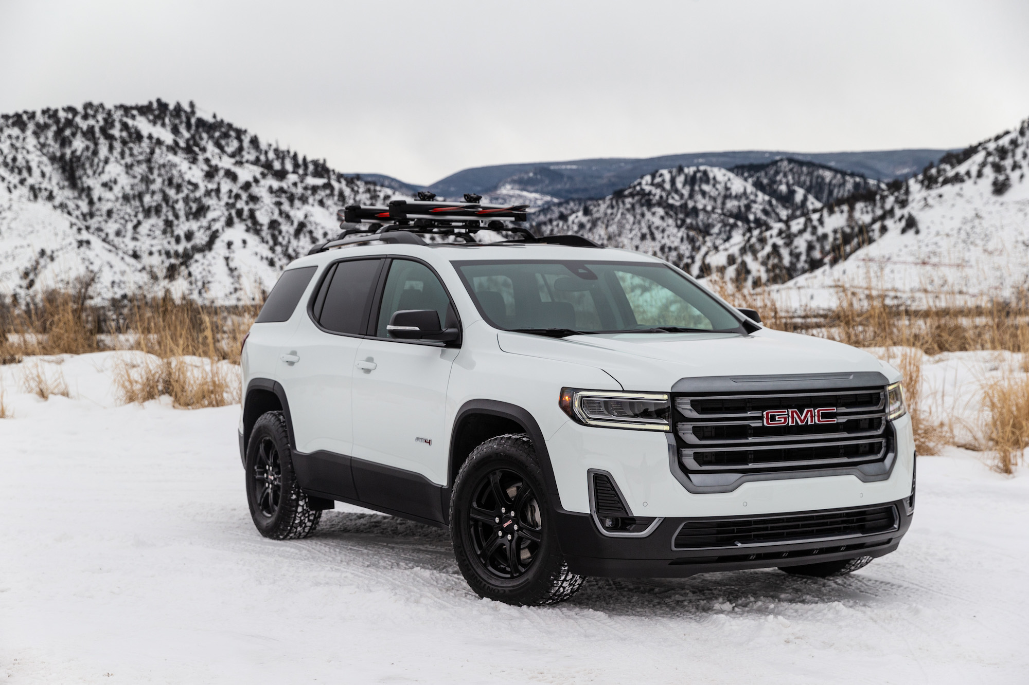 A white 2020 GMC Acadia AT4 parked in the snow in front of mountains