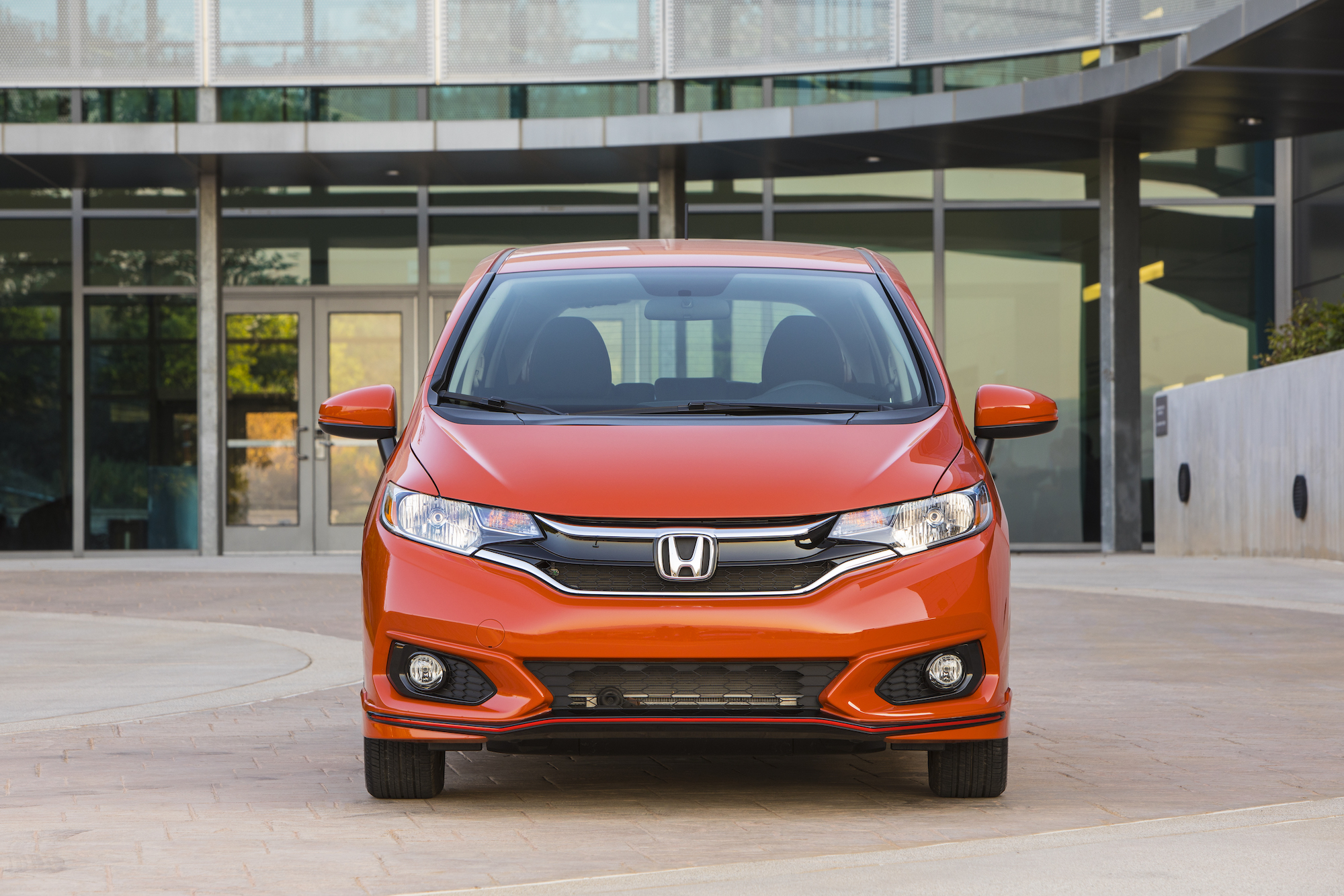 Head-on view of an orange 2020 Honda Fit parked in front of a glass building