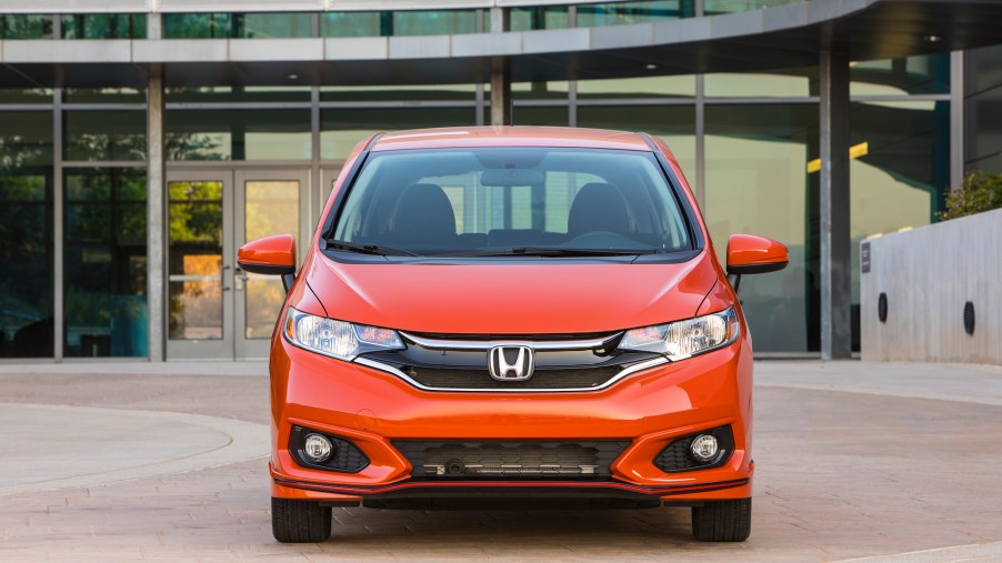 Head-on view of an orange 2020 Honda Fit parked in front of a glass building