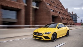 A yellow 2020 Mercedes-Benz CLA 250 4MATIC driving down a city road next to a building