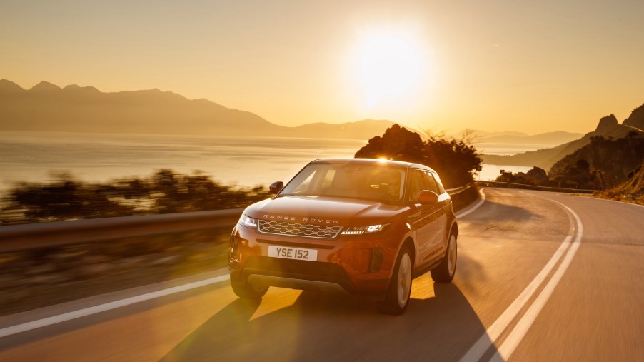 A red 2020 Range Rover Evoque cruises on a paved two-lane road along the water in Greece