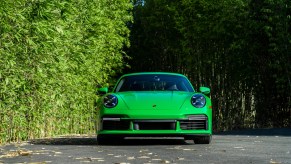 A 2021 Porsche 911 Turbo S in Python Green sits on a paved road next to lush green foliage