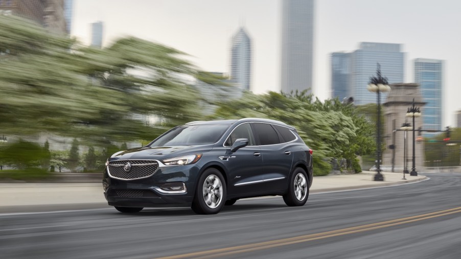 A dark-blue 2021 Buick Enclave midsize crossover SUV travels on a city street lined with trees