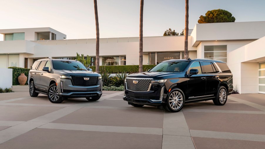 A gray 2021 Cadillac Escalade Sport and a black Premium Luxury parked in front of a large modern white house