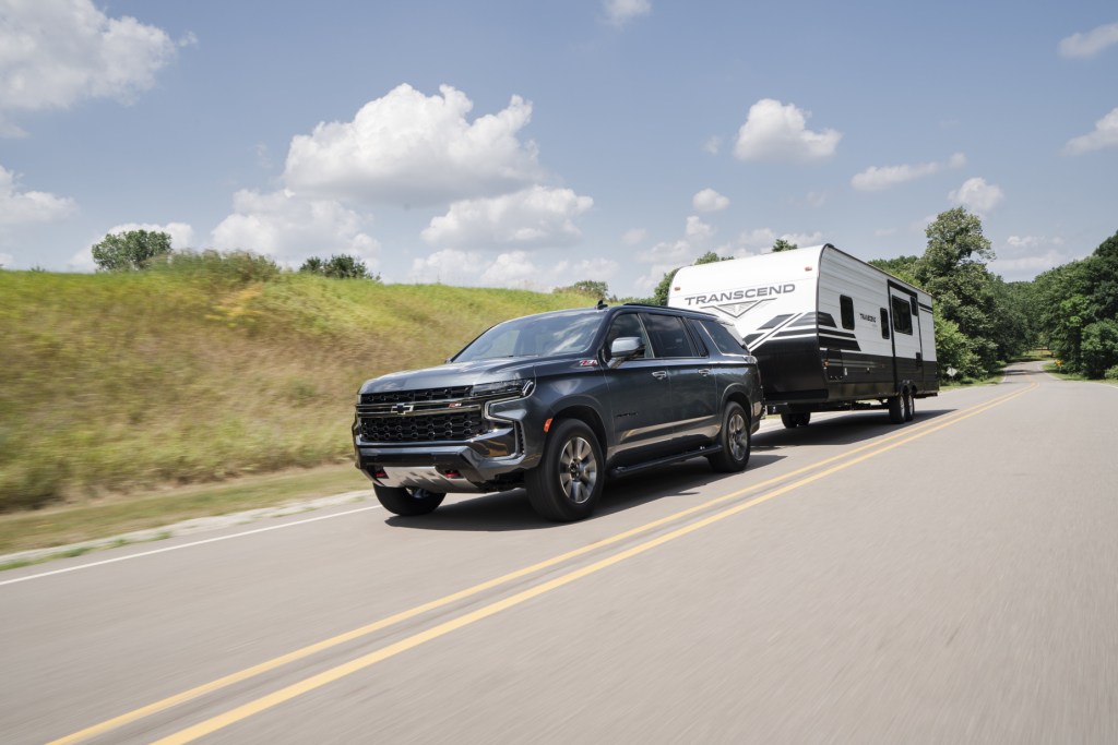 A black 2021 Chevy Suburban large SUV towing a white and blue RV on a highway road
