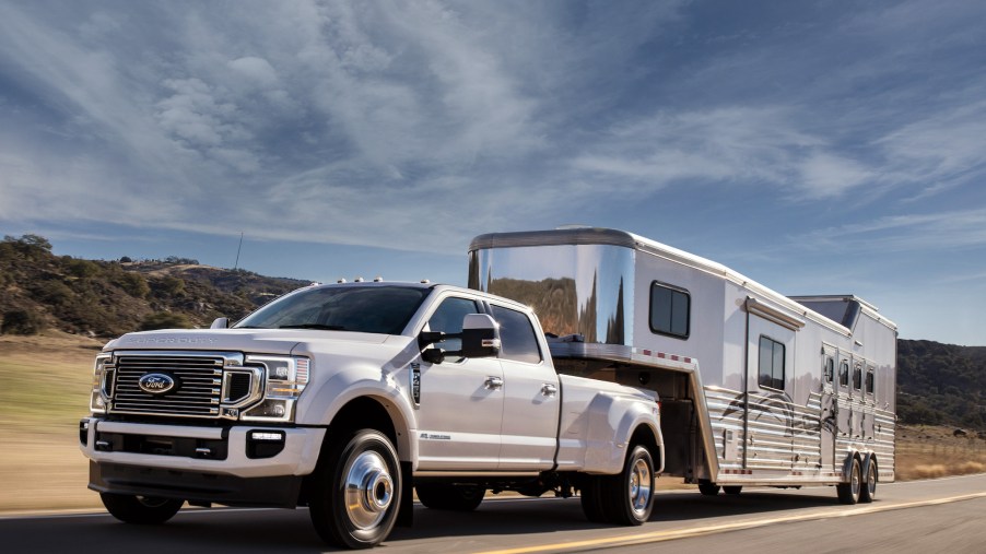 A Ford F-450 Crew Cab 4x4 in Star White Metallic Tinted Clearcoat with FX4 Off-Road Package and available equipment towing a large trailer on the highway