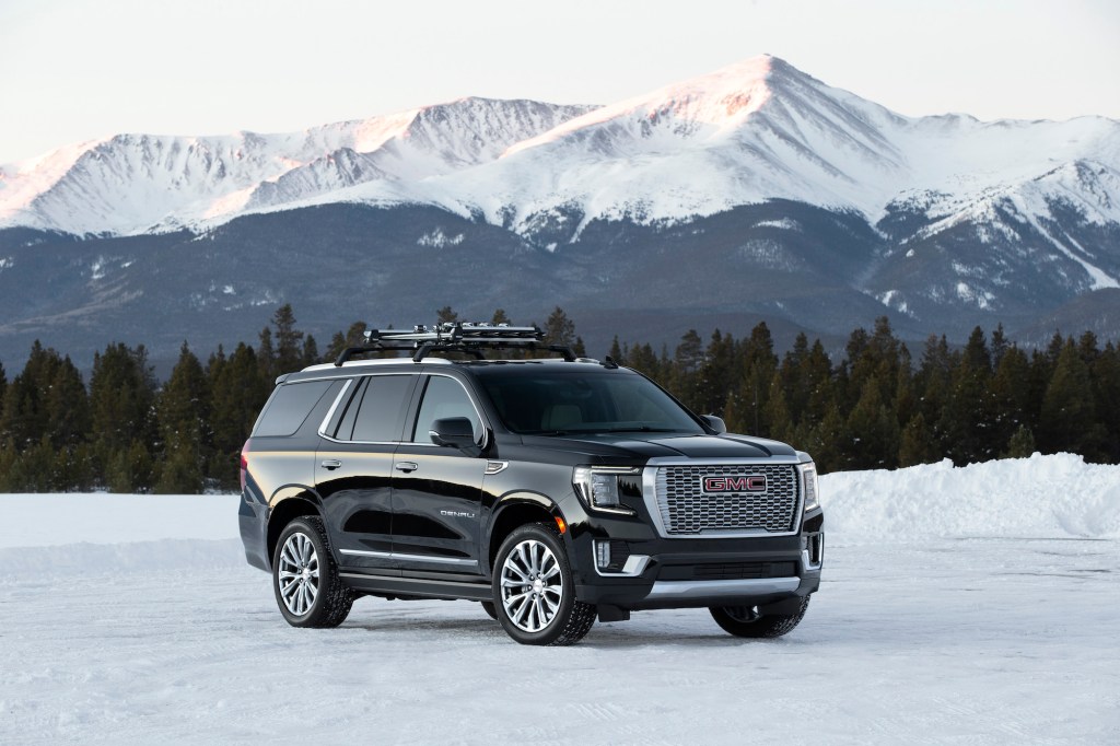 A black 2021 GMC Yukon Denali parked on snow in front of pine trees and snow-capped mountains