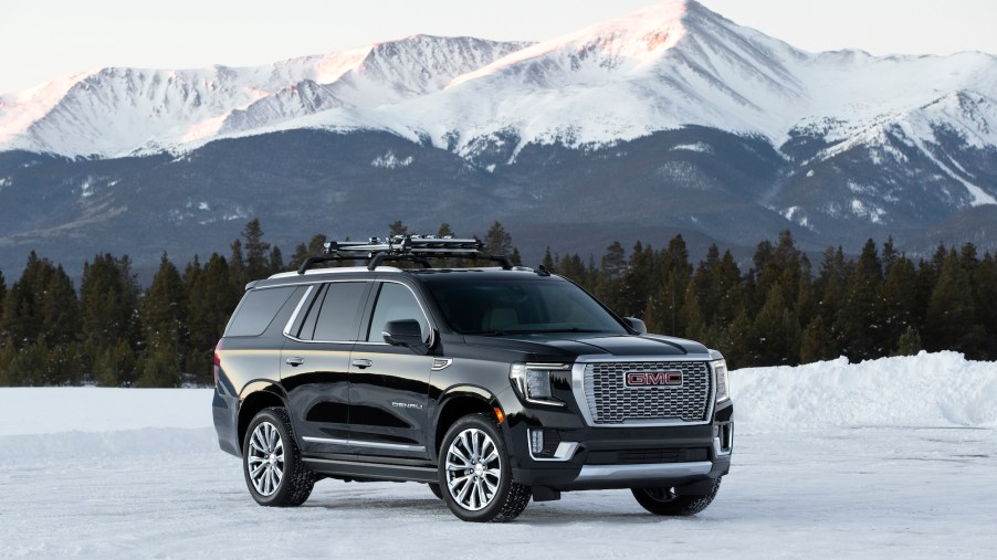A black 2021 GMC Yukon Denali parked on snow in front of pine trees and snow-capped mountains