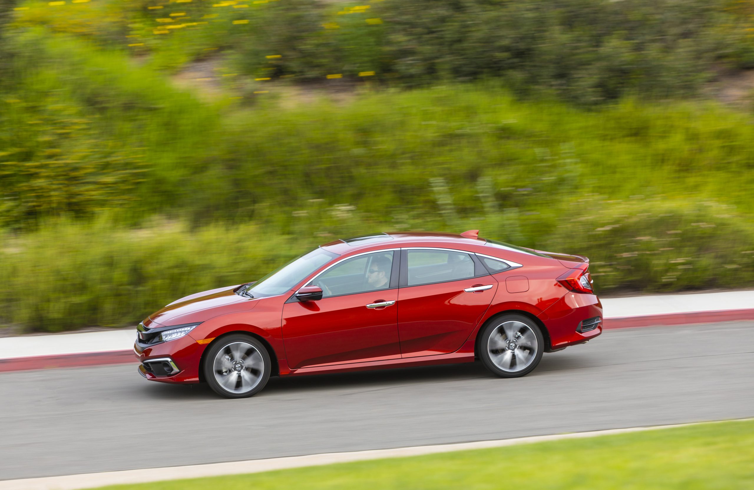 a red Honda Civic model driving at speed on a scenic country road