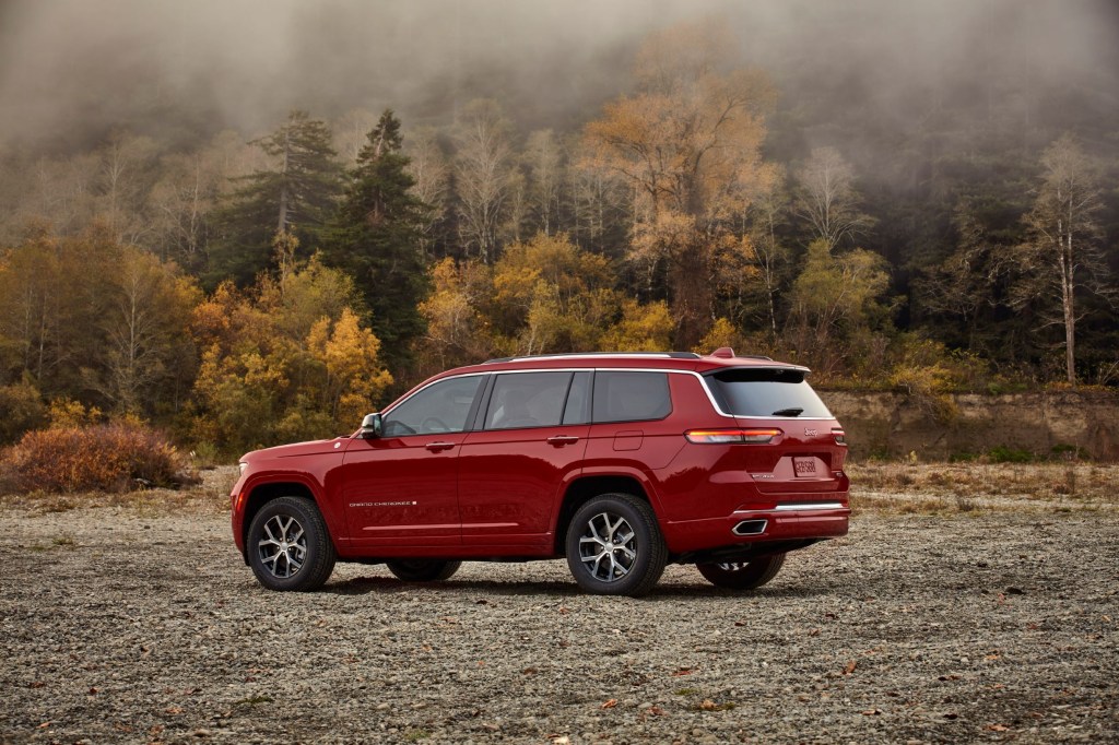 The rear 3/4 view of a red 2021 Jeep Grand Cherokee L Overland by a forest