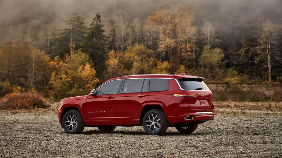 The rear 3/4 view of a red 2021 Jeep Grand Cherokee L Overland by a forest