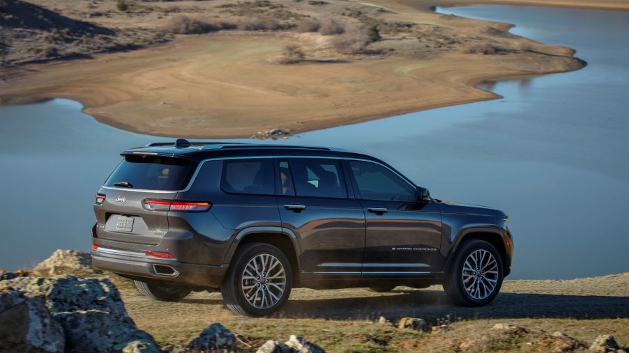 The rear 3/4 view of a brown 2021 Jeep Grand Cherokee L Summit Reserve by a desert lake