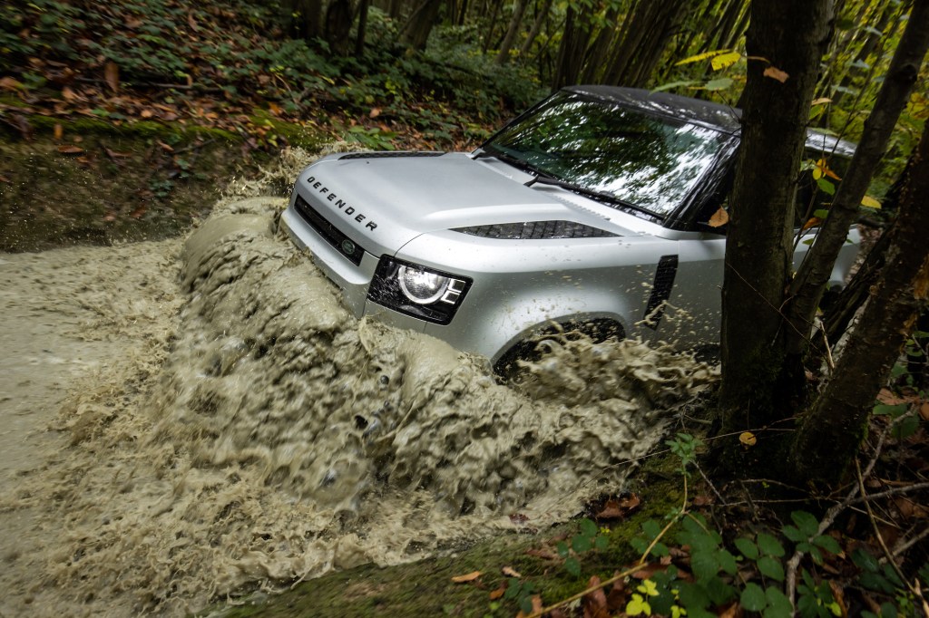 A silver 2021 Land Rover Defender P300 plows through mud