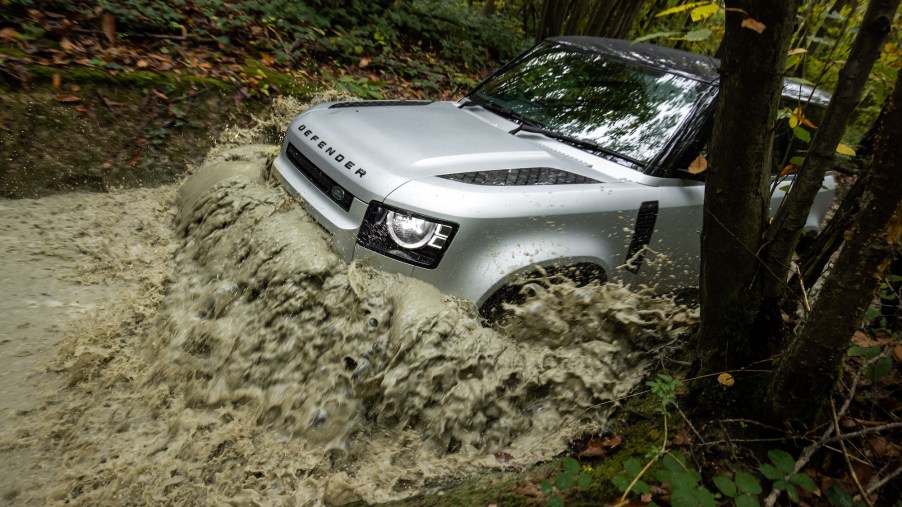 A silver 2021 Land Rover Defender P300 plows through mud