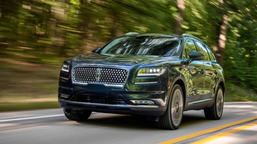 A 2021 Lincoln Nautilus in Flight Blue travels on a two-lane paved road lined by foliage