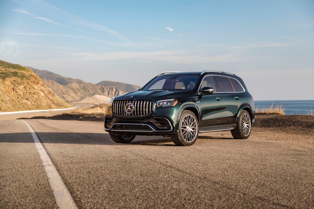 A dark-green 2021 Mercedes-AMG GLS 63 parked on a paved road with blue sky and mountains in the background