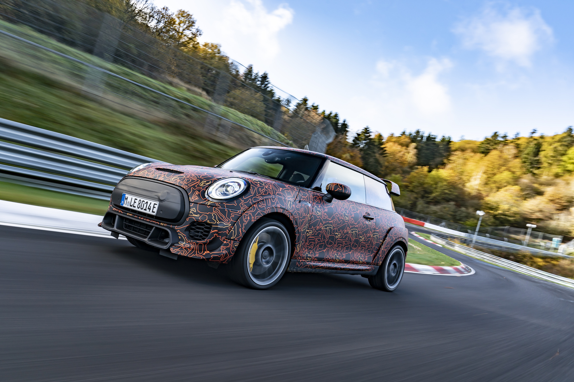 A 2021 Mini John Cooper Works zips around a paved track surrounded by rolling green hills and trees