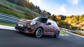 A 2021 Mini John Cooper Works zips around a paved track surrounded by rolling green hills and trees