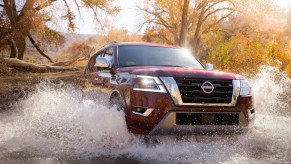A dark-red 2021 Nissan Armada full-size SUV drives across a creek on a sunny day