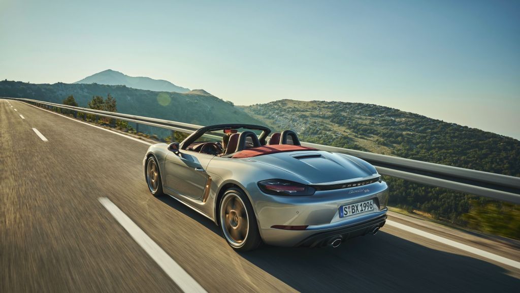 The rear 3/4 view of the silver 2021 Porsche 718 Boxster 25 Years on a mountain road