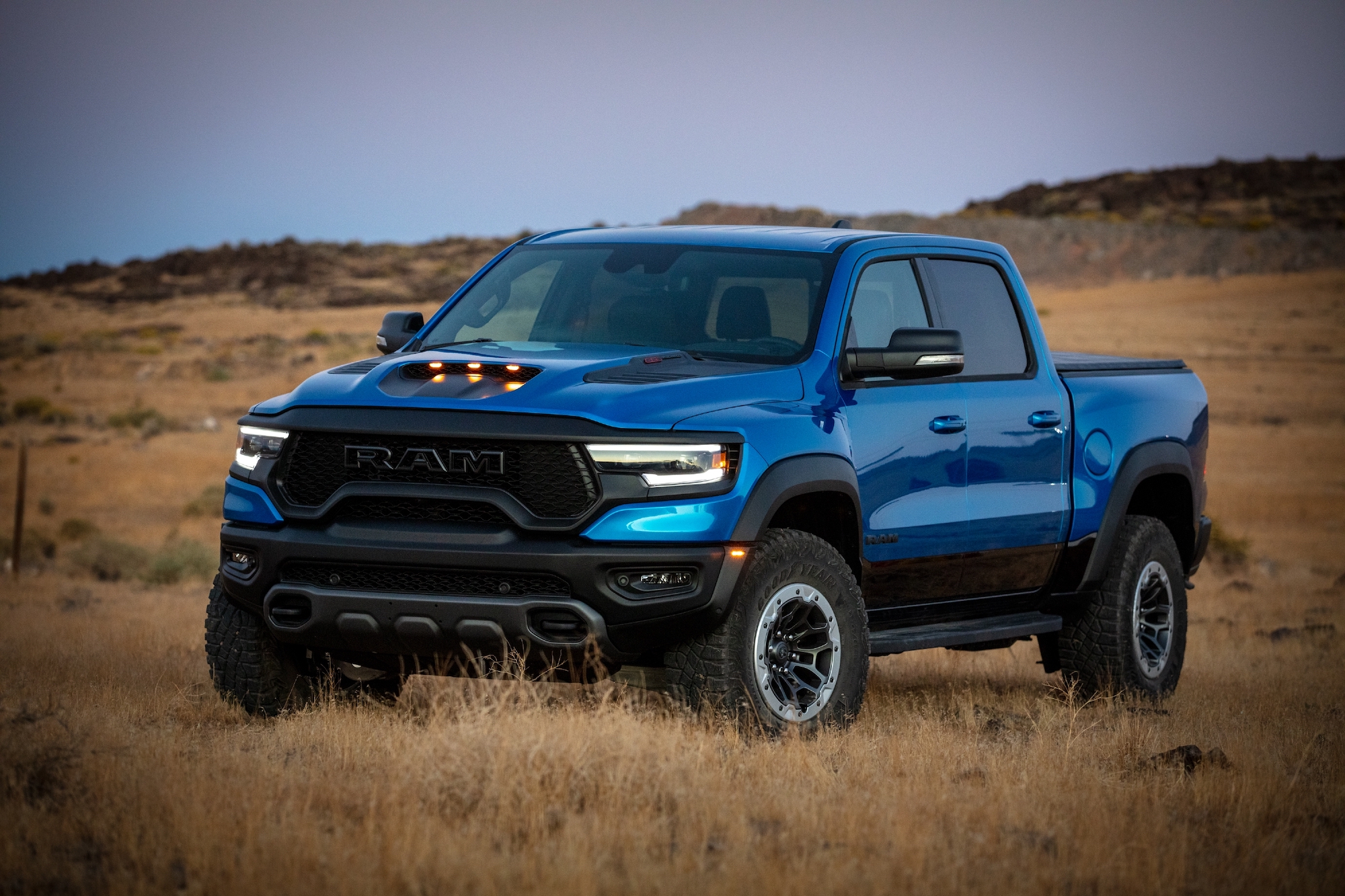 A metallic blue 2021 Ram 1500 TRX parked in a field of brown grass and weeds