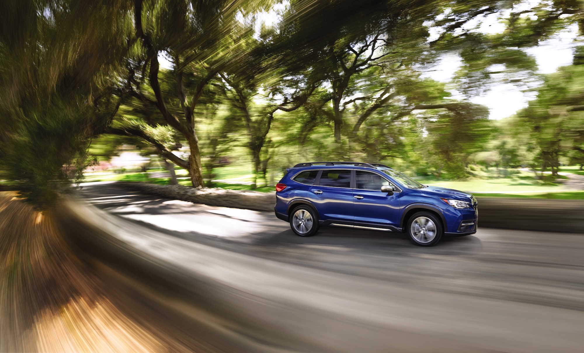 A blue 2021 Subaru Ascent travels on a residential street lined by trees