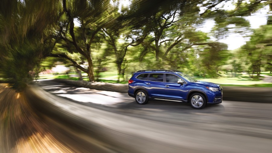 A blue 2021 Subaru Ascent travels on a residential street lined by trees