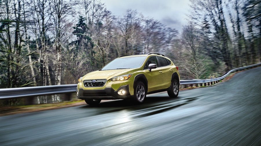 A chartreuse 2021 Subaru Crosstrek Sport Hero travels on a wet paved road along a guardrail and trees