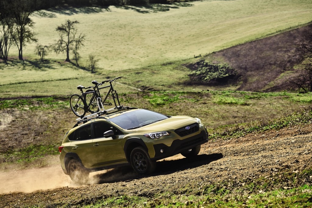 A mustard yellow 2021 Subaru Crosstrek with a bike attached to its roof rack driving down a dirt roat