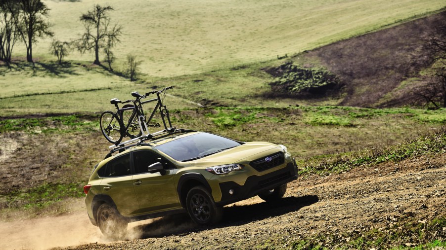 A mustard yellow 2021 Subaru Crosstrek with a bike attached to its roof rack driving down a dirt roat