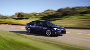 A dark-blue 2021 Subaru Impreza sedan travels on a paved road flanked by grass and bushes