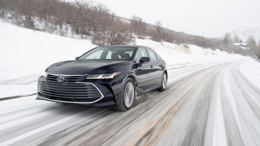 A black 2021 Toyota Avalon Limited AWD traveling on a snowy rural road