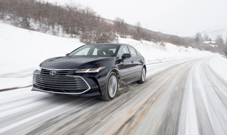 A black 2021 Toyota Avalon Limited AWD traveling on a snowy rural road