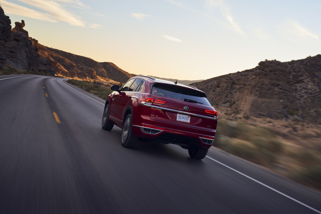 A view of the back end of a red 2021 Volkswagen Atlas Cross Sport driving down a highway road