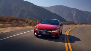 A red 2021 Volkswagen Arteon travels on a two-lane highway through mountains