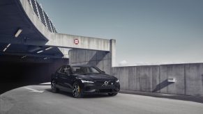 A black 2021 Volvo S60 driving on a road, emerging from the shadows