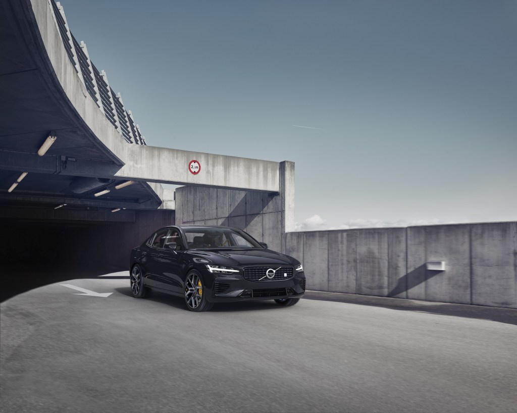 A black 2021 Volvo S60 driving on a road, emerging from the shadows