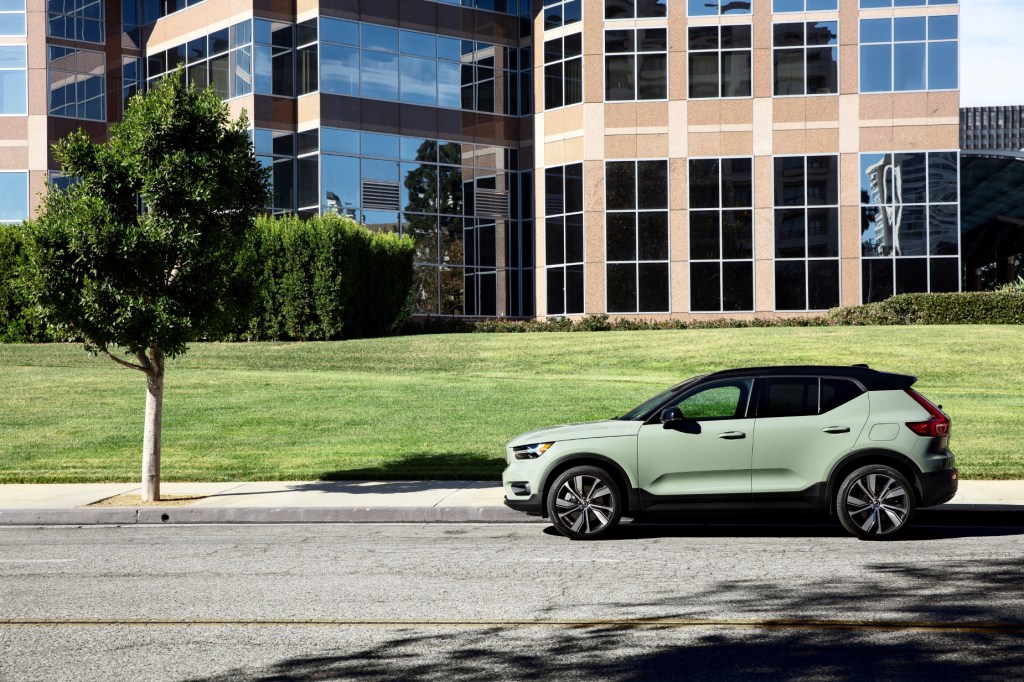 A mint and black 2021 Volvo XC40 Recharge parked on the side of the road with a tree, buldings, and grass in the background