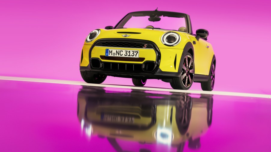 A yellow 2022 Mini Cooper S Convertible on display with a pink background