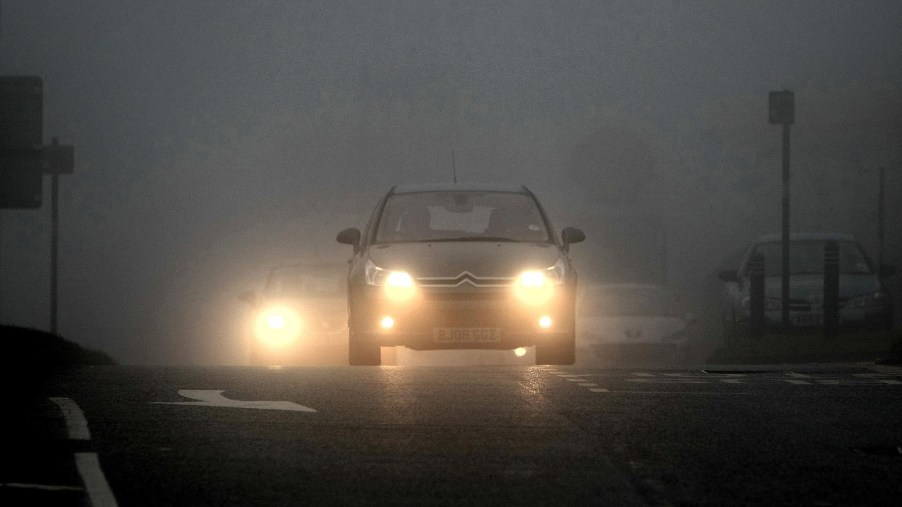 A Citroen with its fog lights on drives on a foggy British roadway