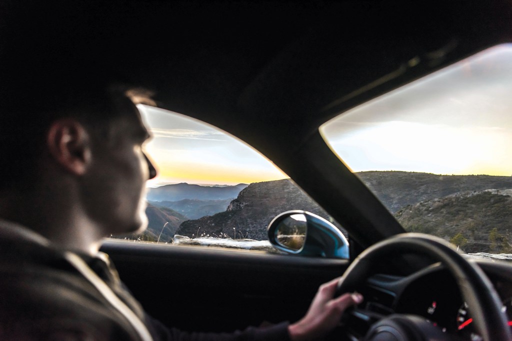 A young man driving a car through the mountains