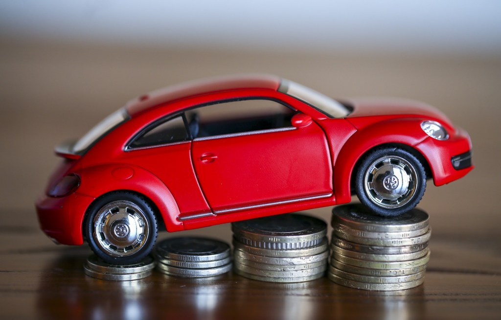 A visual of an auto loan, represented by a red toy Volkswagen bug parked on four ascending stacks of silver coins