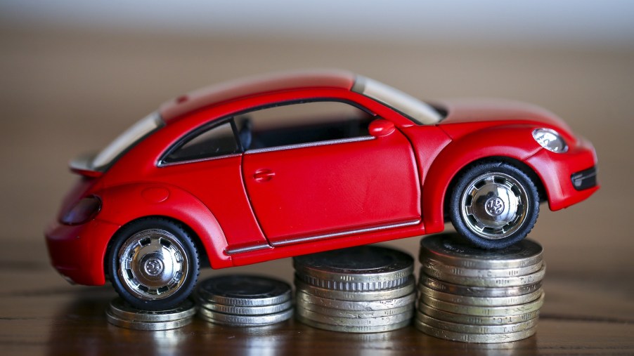 A visual of an auto loan, represented by a red toy Volkswagen bug parked on four ascending stacks of silver coins